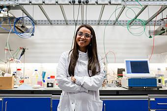 Eine junge Frau in weißem Kittel steht in einem Labor.