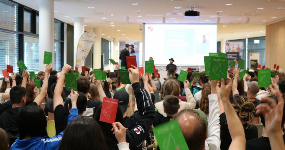 BesucherInnen der Podiumsdiskussion im Rahmen von Innsbruck liest stimmen mit roten und grünen Kärtchen ab.